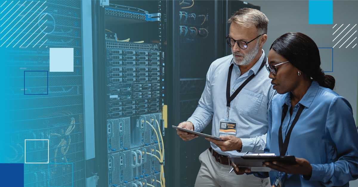 An image of two engineers in a data center inspecting equipment the female engineer is holding a clipboard, the male engineer is holding a tablet