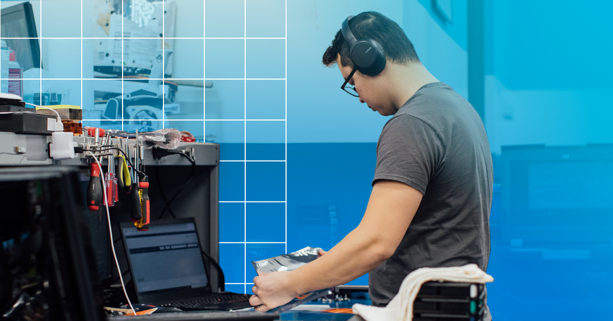 An image of a male engineer wearing headphones at a workbench testing parts